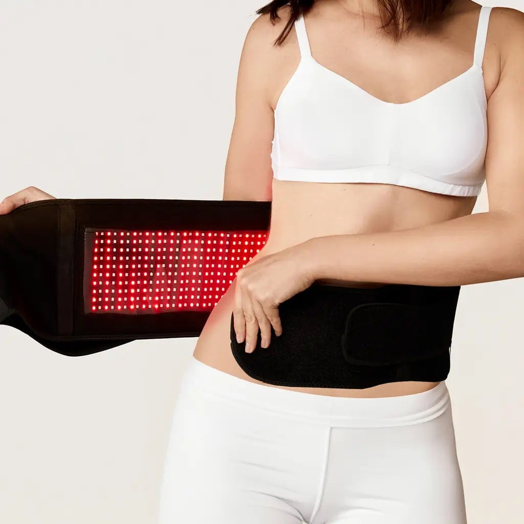 Nushape LipoWrap opened around a woman's waist, its black belt revealing a rectangular panel of glowing red LEDs