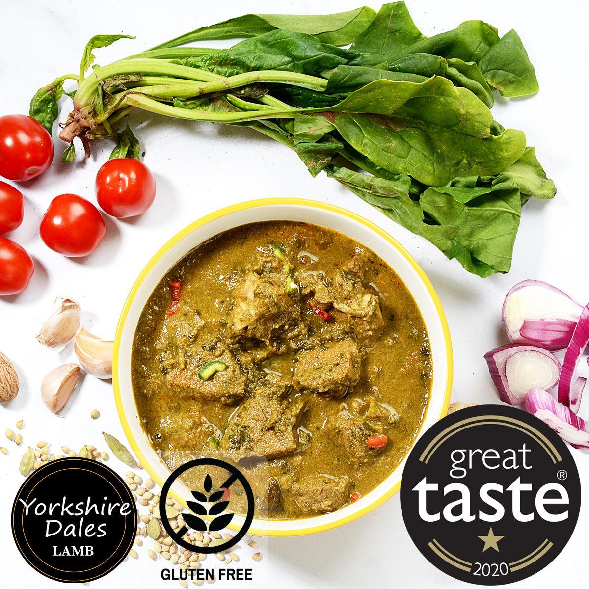 Lamb curry with cardamom pods and sliced onions in yellow bowl, surrounded by fresh spinach and tomatoes